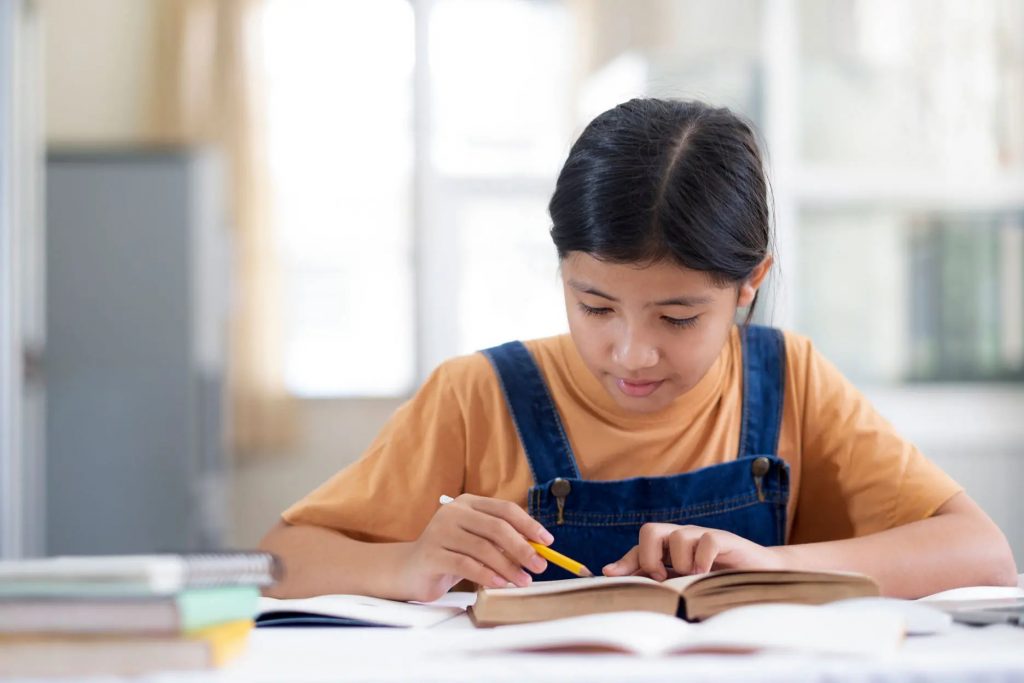 A girl sitting at a desk, studying and writing notes in her notebook.
