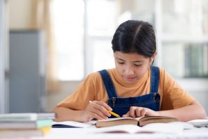 A girl sitting at a desk, studying and writing notes in her notebook.