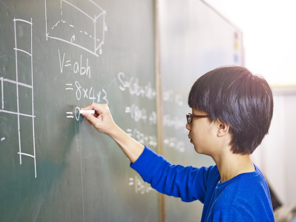 A young boy solving Math equations on a classroom board