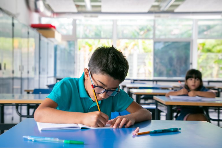 Boy with glasses writing in classroom