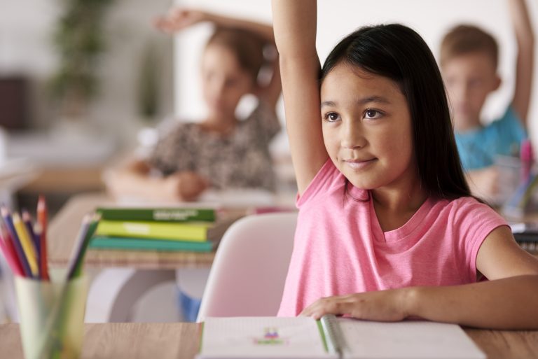 Girl raising hand to answer question in classroom