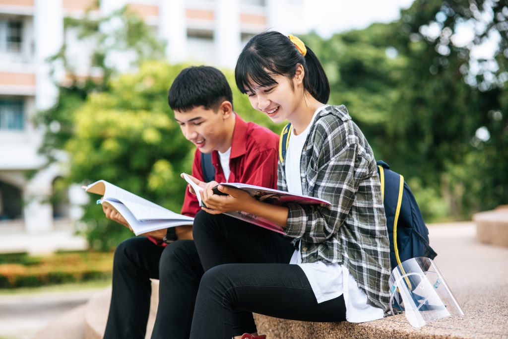 Male and female students sitting and reading books on the stairs