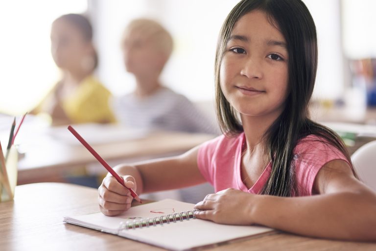 Asian schoolgirl sitting at desk and writing in a notebook during class