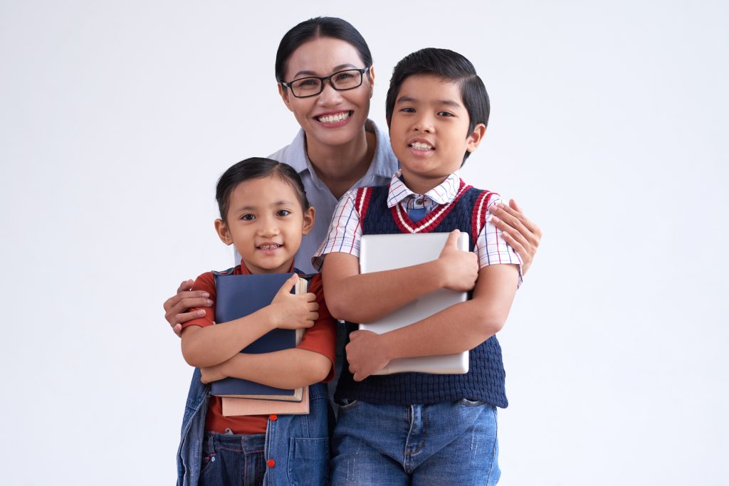 Asian woman hugging two young school children