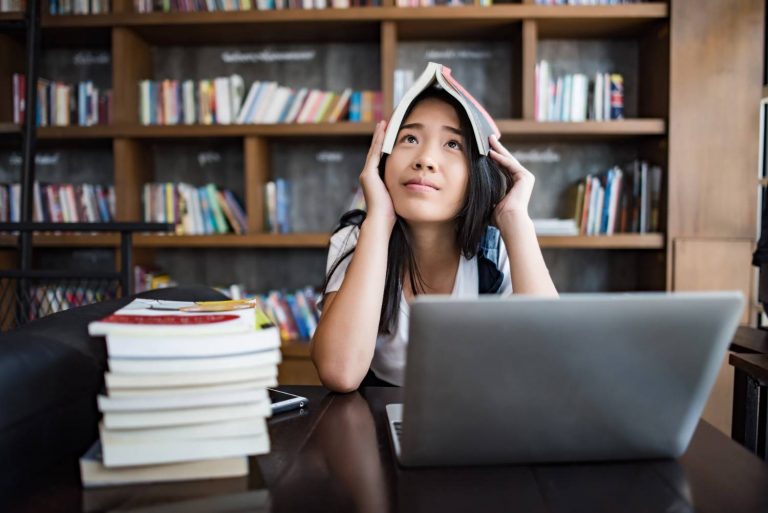 A stressed student sitting in a library with a book on her head