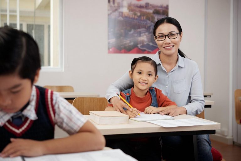 Female teacher with glasses helping young student with schoolwork in classroom