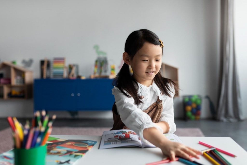 Smiling young girl engaged in coloring activity with colored pencils and book