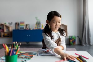 Smiling young girl engaged in coloring activity with colored pencils and book