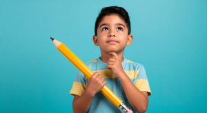 Young boy in striped shirt looking up thoughtfully while holding large yellow pencil