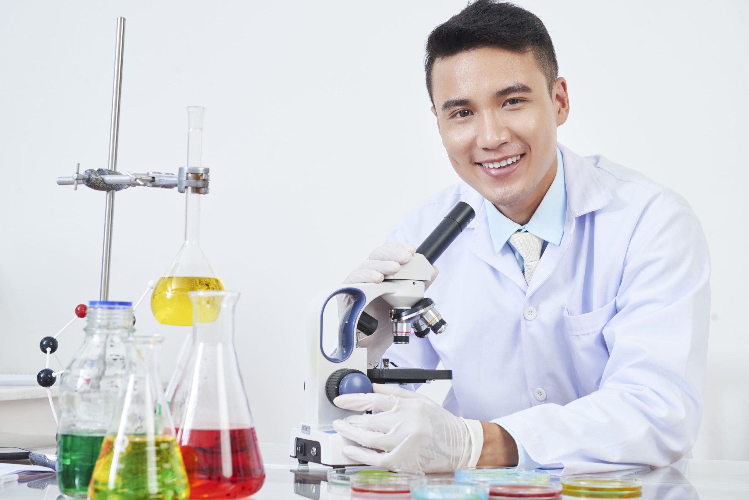 Student in a lab coat smiling next to a microscope