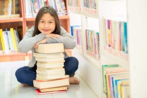 Young student sitting in library with a stack of books